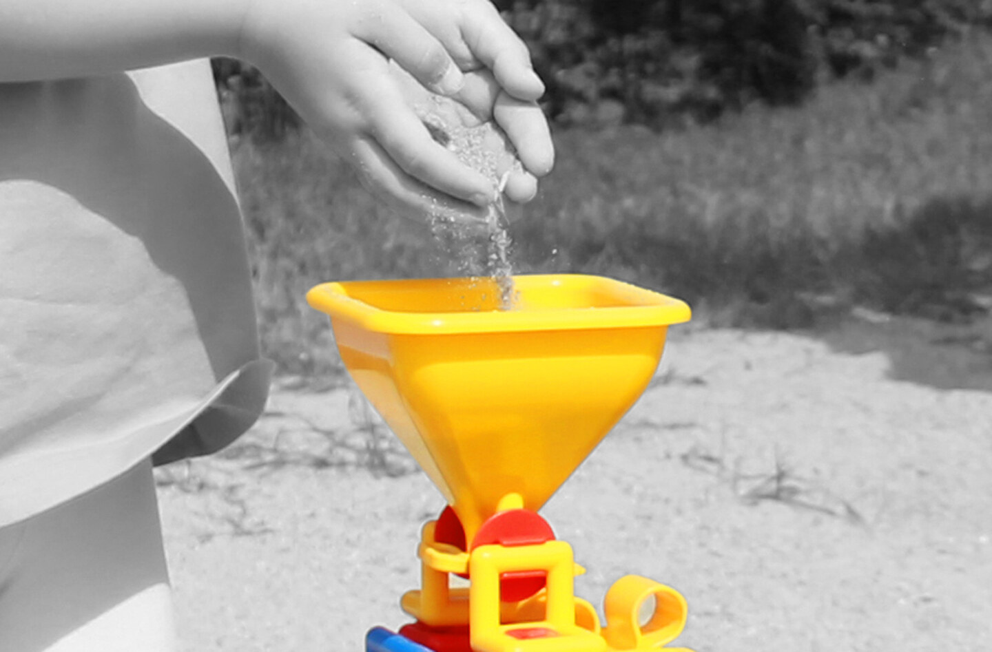 Les mains d'un enfant remplissant le sable dans un entonnoir jaune de plasticant mobilo